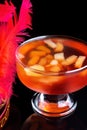 Orange jello on a beautiful bowl with fruit pieces inside. Black background, decorated with pink feathers.