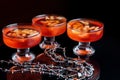 Orange jello on a beautiful bowl with fruit pieces inside. Black background, three vases with jelly.