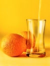 Orange juice being poured into a clear lass beside two oranges