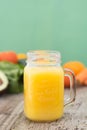 Orange juice and carrot juice, in the glass jar. Green background. Rustic wooden table. Healthy, vegan food and drinks Royalty Free Stock Photo