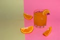 orange juice and drinking glass on a pastel pink-olive background, eye cup three slice orange, cold healthy summer refreshment