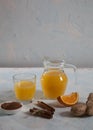 Orange juice with ginger in a glass jug and in a glass, cinnamon sticks on a light background. Health. Copy spaes