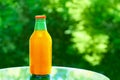 Orange juice in a glass bottle on a mirrored tabletop in the summer outdoors against background of green foliage