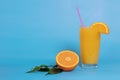 Orange juice in a glass with a straw, decorated with a slice of orange, half an orange with leaves on a blue background Royalty Free Stock Photo