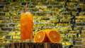 Orange juice in a glass with a straw in a transparent glass on a brick wall background. Yellow lemonade with ice Royalty Free Stock Photo