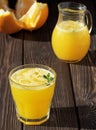 Orange juice in the glass wiht leaf mint and pices of ice on the dark wood board. Near orange and jug of orange juice. Soft focus Royalty Free Stock Photo