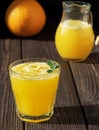 Orange juice in the glass wiht leaf mint and pices of ice on the dark wood board. Near orange and jug of orange juice. Soft focus Royalty Free Stock Photo