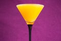 Orange juice in a martini glass on a violet background