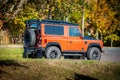 An orange Land Rover Defender parked on the road in autumn