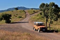 Orange Land Rover Defender in a path, trees, and mountains with blue sky in the background