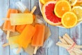 Orange, lemon and grapefruit ice pops, overhead scene on wood