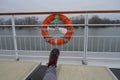 Orange life belt at the railing of a ship floating in a river . Neutral foot of a tourist points toward the ring . visible rescue Royalty Free Stock Photo