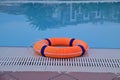 An orange life buoy rests on the edge of a blue water pool Royalty Free Stock Photo