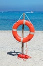 Orange life buoy on the sandy beach against blue sea water Royalty Free Stock Photo