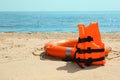 Orange life jacket and buoy on sandy beach near sea. Emergency rescue equipment Royalty Free Stock Photo