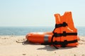 Orange life jacket and buoy on sandy beach near sea. Emergency rescue equipment Royalty Free Stock Photo