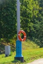 Orange lifebuoy hanging on a rope on a metal pole on a background of trees Royalty Free Stock Photo