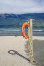 An orange lifebuoy hanging on a wooden pole on a beach near a lake shore Royalty Free Stock Photo