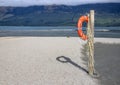 An orange lifebuoy hanging on a wooden pole on a beach near a lake shore Royalty Free Stock Photo