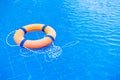 Orange lifebuoy pool ring float on blue water. Life ring in swimming pool, life ring floating on top of sunny blue water Royalty Free Stock Photo