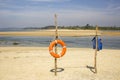 Orange lifebuoy ring and blue life vest on a bamboo stand on a sandy beach against the backdrop of the sea bay and green jungle Royalty Free Stock Photo