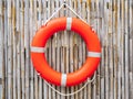 An orange lifebuoy, safety ring hanging on bamboo fence wall background. Royalty Free Stock Photo