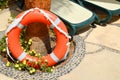 The orange lifebuoy for safety of swimming rests on a stone floor against a background of yellow flowers and sun loungers Royalty Free Stock Photo