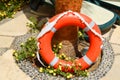 The orange lifebuoy for safety of swimming rests on a stone floor against a background of yellow flowers and sun loungers Royalty Free Stock Photo