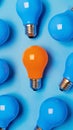 Orange light bulb surrounded by blue light bulbs on a blue background. Concept of standing out and creativity Royalty Free Stock Photo