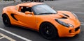 an orange lotus sports car parked in a parking lot near several other cars