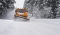 Orange maintenance plough truck on forest road after snowstorm blizzard. Roads get dangerous during winter driver face