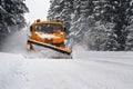 Orange maintenance plough truck on forest road after snowstorm blizzard. Roads get dangerous during winter