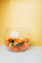 Orange mandarins clementine with green leaves in round clear vase on a white-yellow background