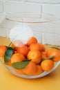 Orange mandarins clementine with green leaves in round clear vase on a white-yellow background