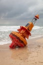 An orange marine buoy unmoored and washed up on a beach after a hurricane.