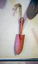 Orange metal spade tool or shovel hanging against brown wall.