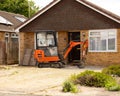 Orange mini excavator digger clearing driveway in front of bungalow