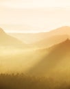 Orange misty morning, view over rock to deep valley full of light mist. Dreamy spring landscape within daybreak