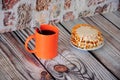 An orange mug of black coffee and a plate with flat waffles and white syrup
