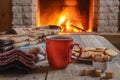 Orange mug for tea or coffee; wool things near cozy fireplace. Royalty Free Stock Photo