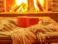 Orange mugs for tea or coffee; wool things near cozy fireplace.