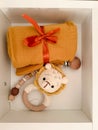 An orange muslin diaper tied with a ribbon, a rattle in the form of a lion, a teether made of wooden beads.