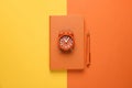 Orange notebook, alarm clock and pen on background, top view