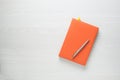 Orange notepad with a pen on white wooden background