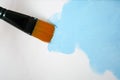 Orange paintbrush drawing light blue color on canvas. Art, painting concept.