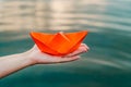 An orange paper ship in a female hand over the water. Woman& x27;s hand holding paper boat above the water. Close-up Royalty Free Stock Photo