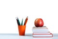 Orange pencil holder, stack of books on white table with red apple isolated on a white background, back to school education Royalty Free Stock Photo