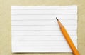 Orange pencil on a scrap of empty paper in a strip for notes on a cardboard background, concept back to school