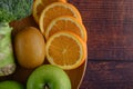 Orange pieces, apple, kiwi, and Broccoli on a wooden plate