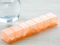 Orange pill box and glass of water. Prescription drugs in seven day pill case. Royalty Free Stock Photo